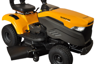 Trator cortador de grama amarelo com motor frontal, assento elevado e deck de corte lateral, recomendado para propriedades rurais, chácaras e jardins extensos.
